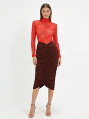 Woman wearing a red sheer top and brown ruched skirt on a white background