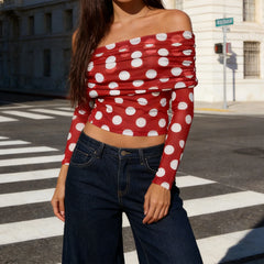 Person wearing a red polka dot top and blue jeans on a city street.