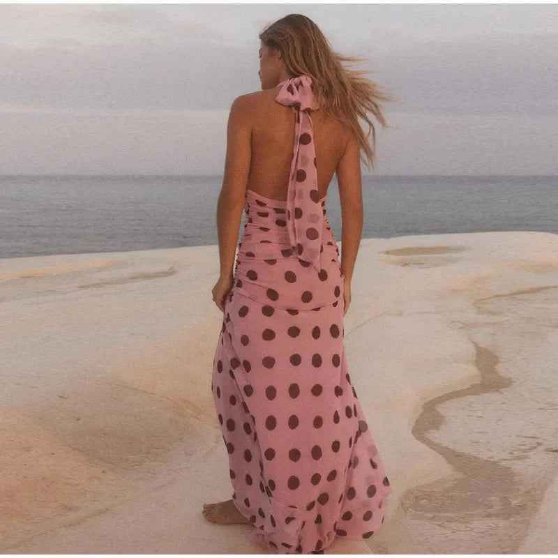 Woman in a pink polka dot dress standing on a beach with ocean view