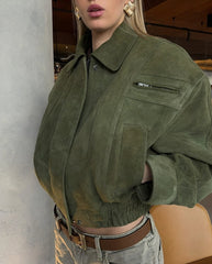 Person wearing a green suede jacket with a neutral background