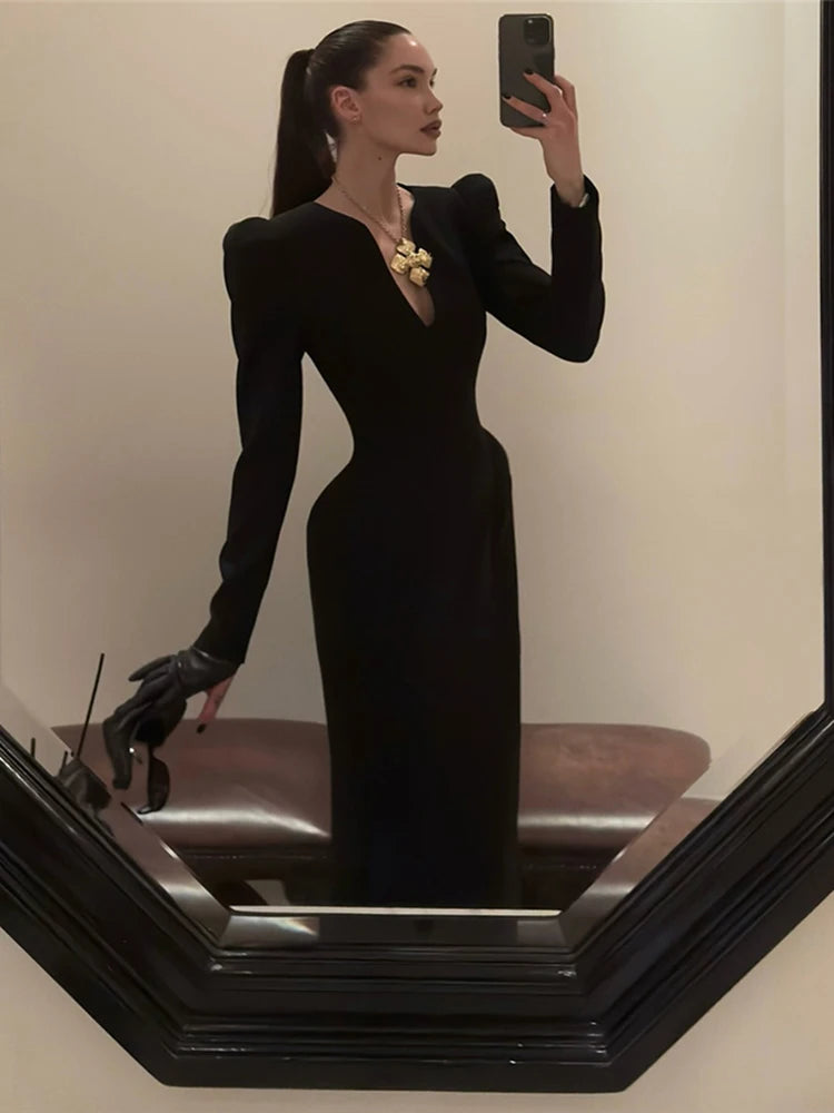 Woman in a black dress taking a mirror selfie.
