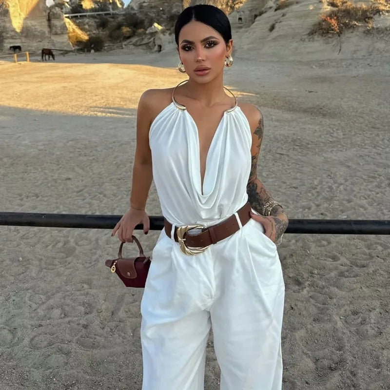 Woman in a white outfit with a brown belt and handbag standing in a desert-like setting.
