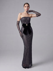 Woman wearing a black strapless gown with a bow and long gloves on a gray background