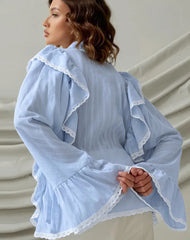 Woman wearing a light blue dress with ruffled details against a neutral background