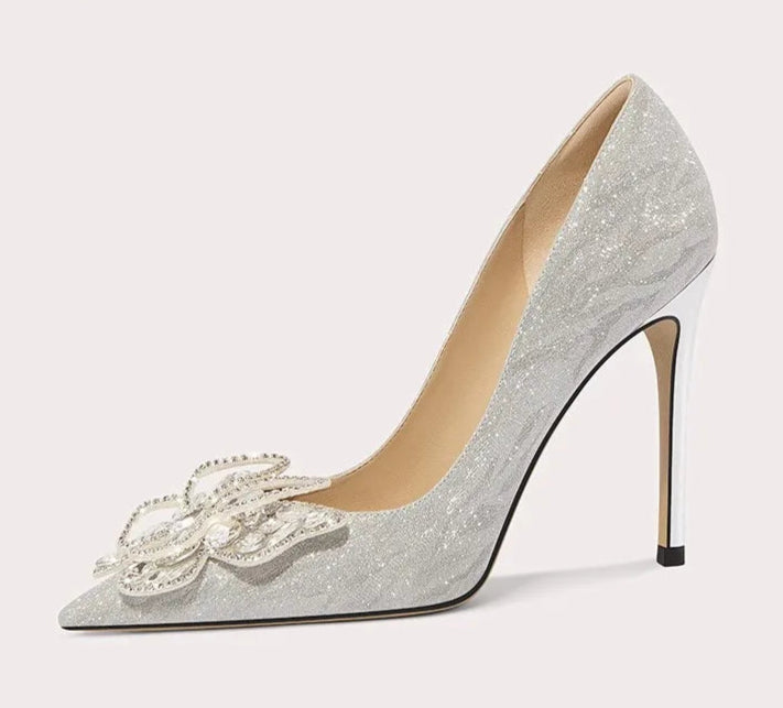 Silver high-heeled shoe with decorative bow on a light gray background