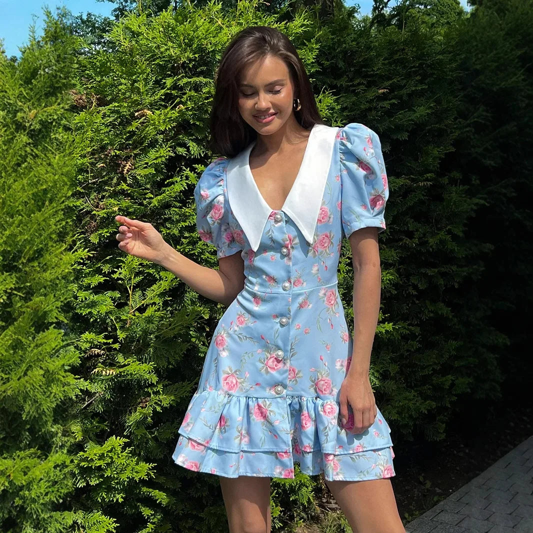 Woman wearing a blue floral dress with a white collar in an outdoor setting.