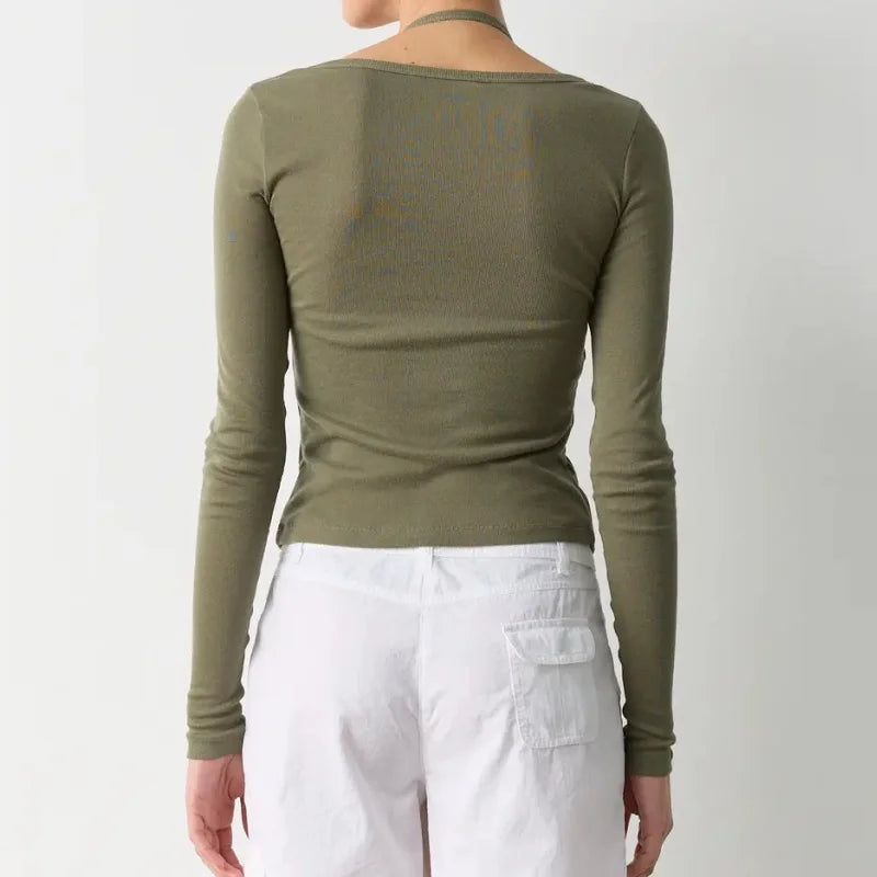 Person wearing an olive green long-sleeve top and white pants on a plain background