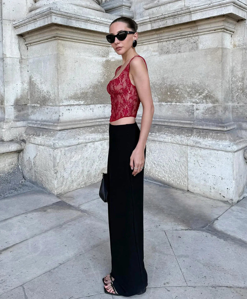 Woman in a red lace top and black skirt standing against a stone wall.