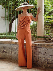 Woman in an orange outfit with ruffled top and wide-leg pants, standing outdoors.