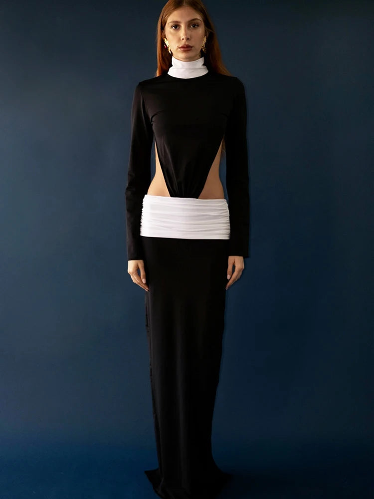 Person wearing a black long-sleeve top with cut-out design and white waistband, standing against a dark blue background.