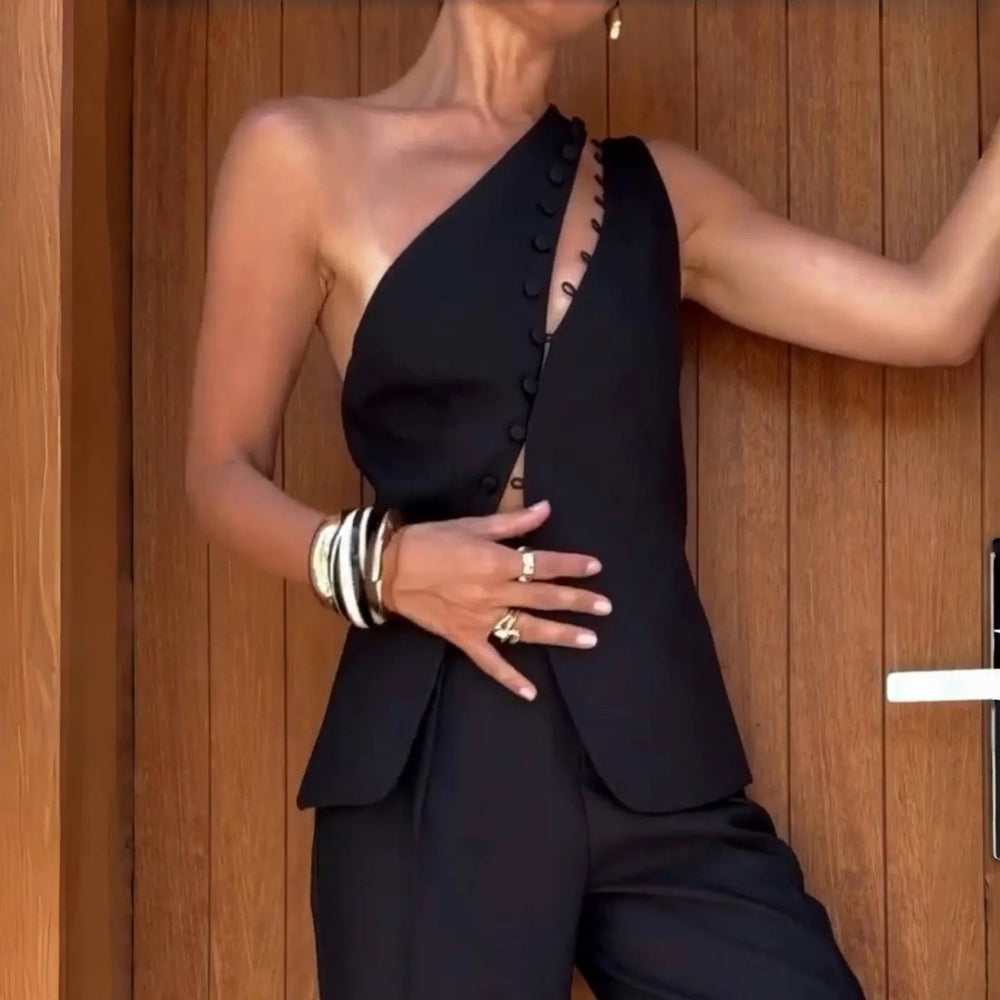 Person wearing a black one-shoulder outfit with buttons against a wooden background