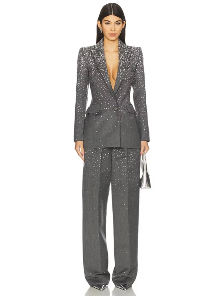 Model wearing a grey crystal-embellished blazer and matching wide-leg pants, holding a silver handbag.