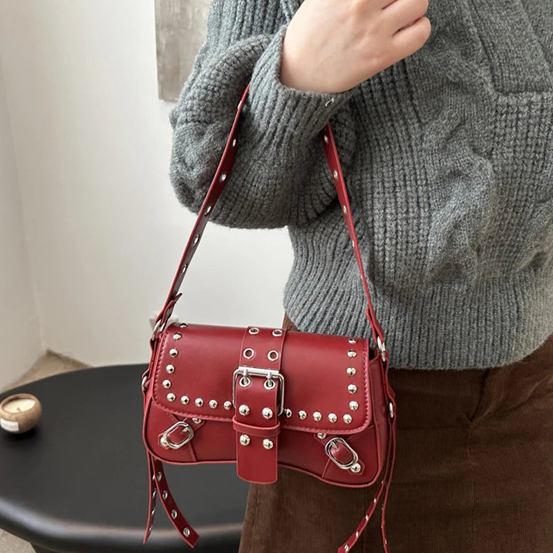 Red studded handbag held by a person wearing a gray sweater.