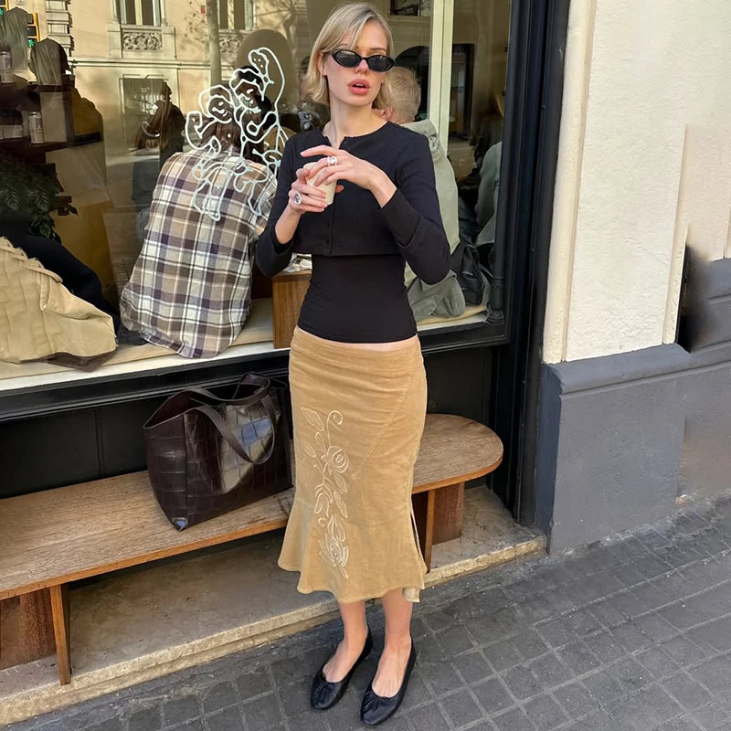 Woman taking a selfie in front of a store window with bags displayed.