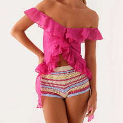 Woman wearing a bright pink off-shoulder top and colorful striped shorts on a white background