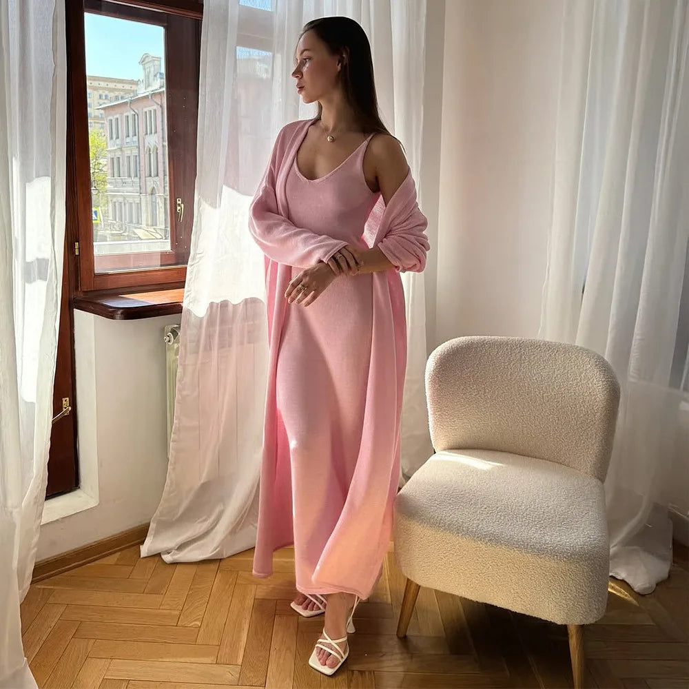 Woman in a pink dress standing in a room with white curtains and a chair.