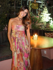 Woman in a floral dress standing in an indoor setting with plants and a candle.