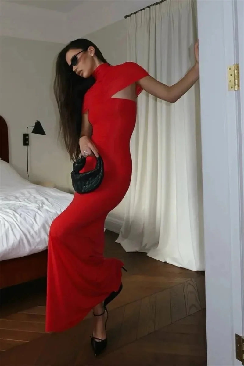 Woman in a red dress holding a black handbag in a bedroom setting.