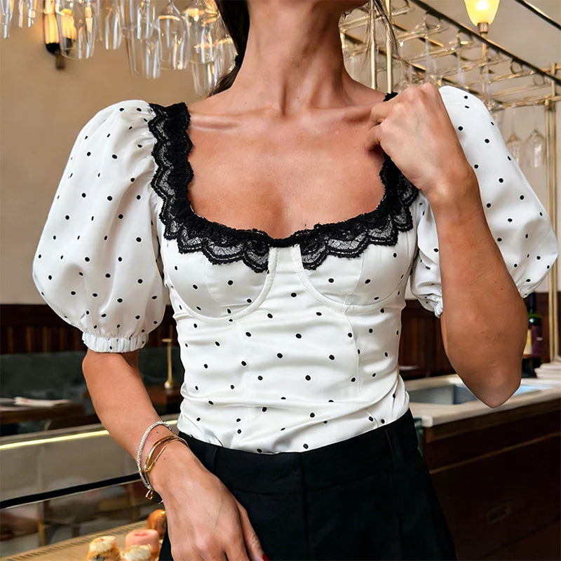 Woman wearing a white blouse with black polka dots and lace details in an indoor setting.