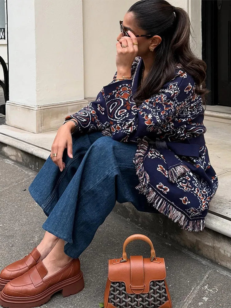 Woman sitting on a step wearing a patterned shirt, jeans, and brown shoes with a brown handbag.