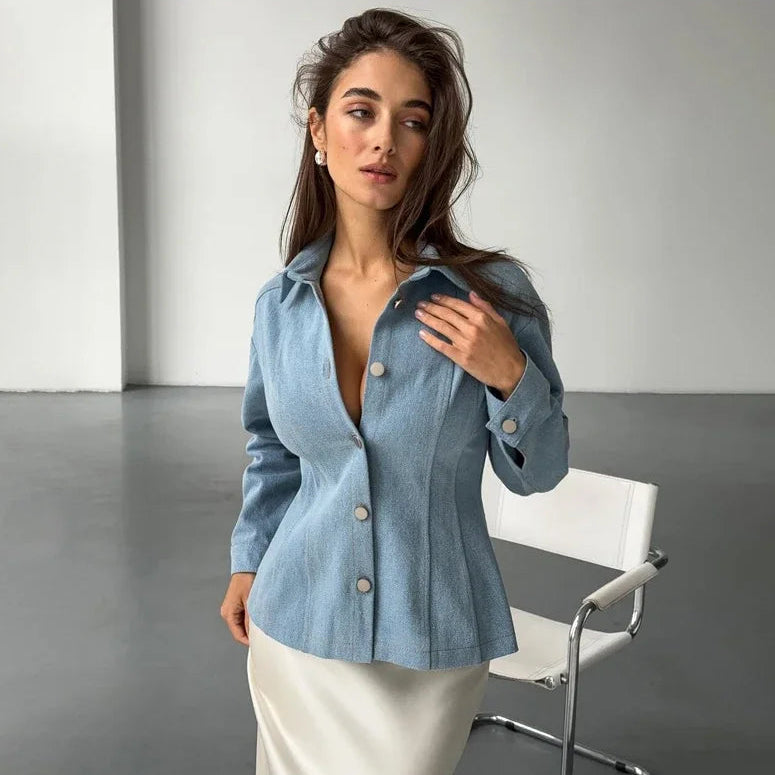 Woman wearing a blue denim jacket over a white top in a minimalistic setting.