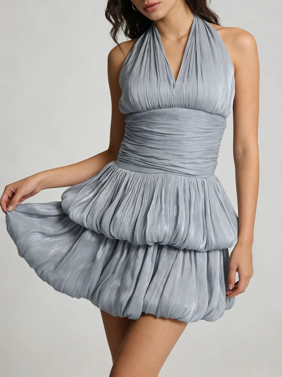 A woman wearing a blue pleated dress against a plain background