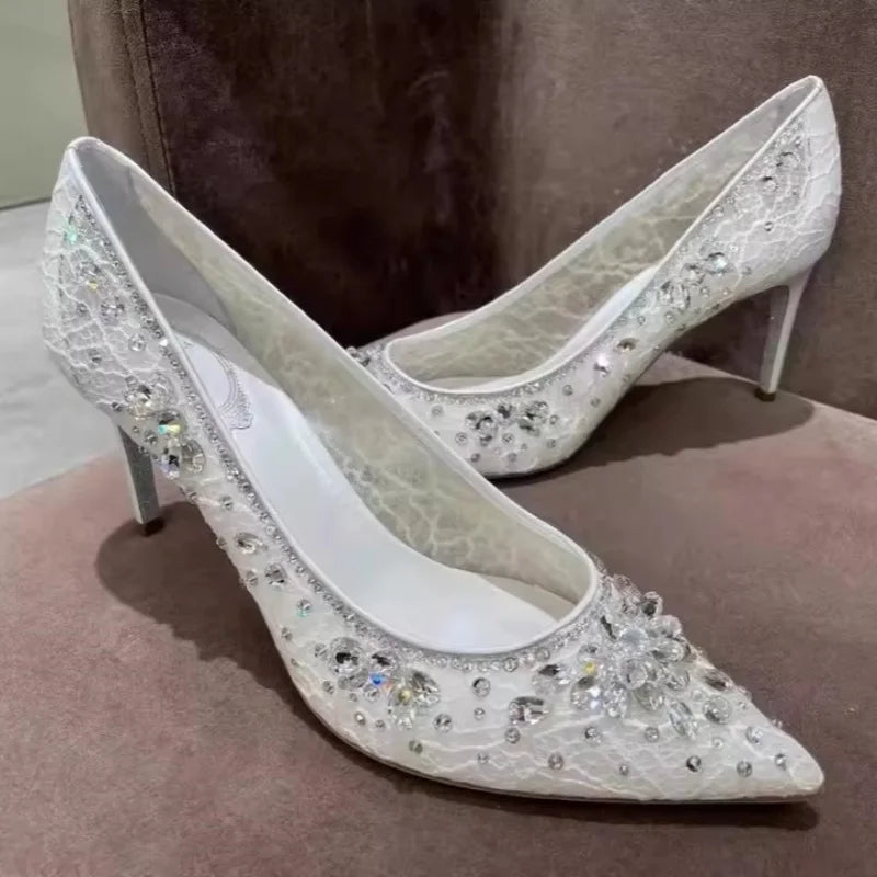 White high-heeled shoes with crystal embellishments on a brown surface