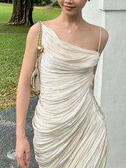 A woman wearing a beige one-shoulder dress with a gold handbag outdoors.