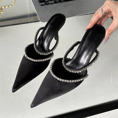 Black pointed-toe-heeled shoes with rhinestone embellishments on a reflective surface