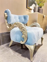 Decorative chair with light blue velvet upholstery and gold ornate legs in a room setting.
