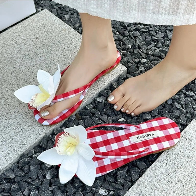 Red and white checkered flip-flops with floral decorations on a stone surface.