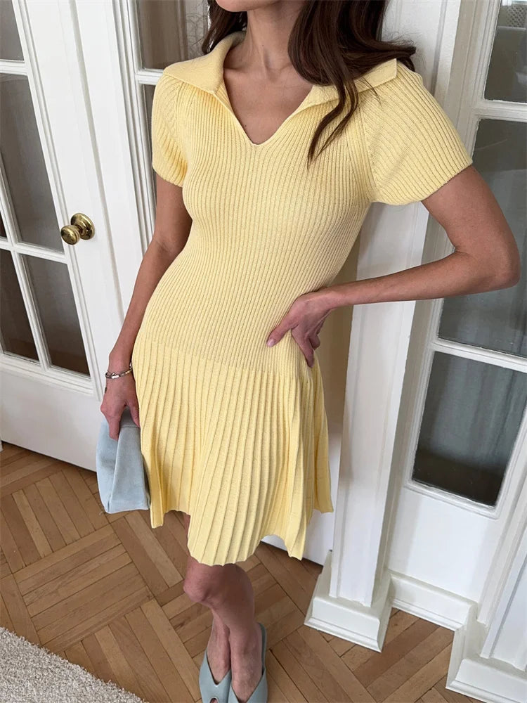 Woman wearing a yellow ribbed dress standing indoors.