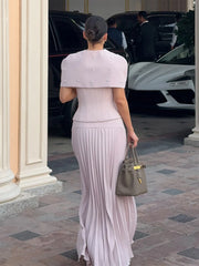 Woman in a light purple dress with a matching jacket walking away from the camera, with cars and people in the background.
