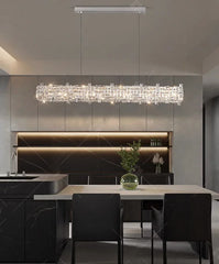 Modern kitchen with a long rectangular chandelier, black chairs, and a marble countertop.