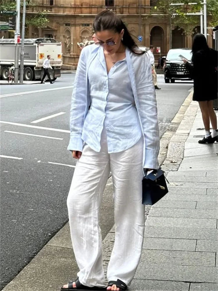 Woman in a light blue blazer and white pants walking on a city street.