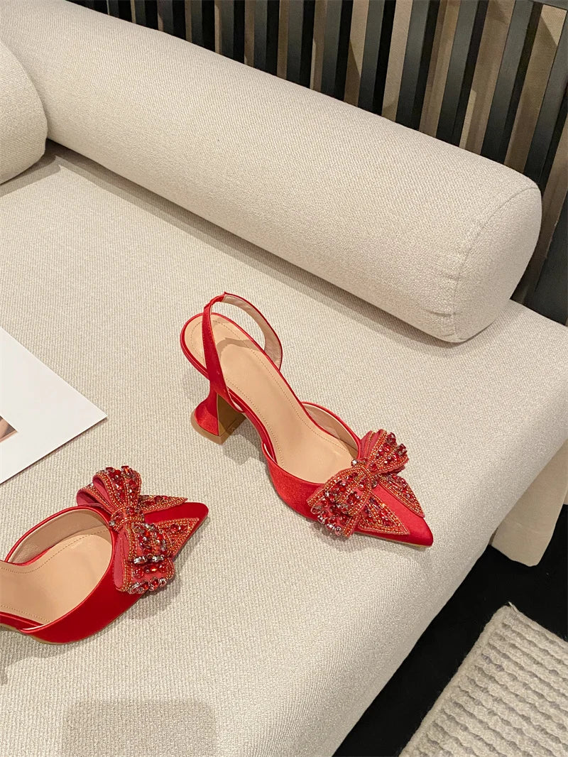 Red high-heeled shoes with decorative bows on a beige sofa.