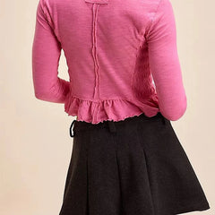 Person wearing a pink blouse with ruffled details and a black skirt on a beige background