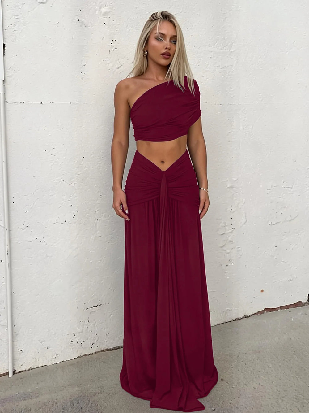 Model wearing a burgundy one-shoulder ruched crop top and maxi skirt