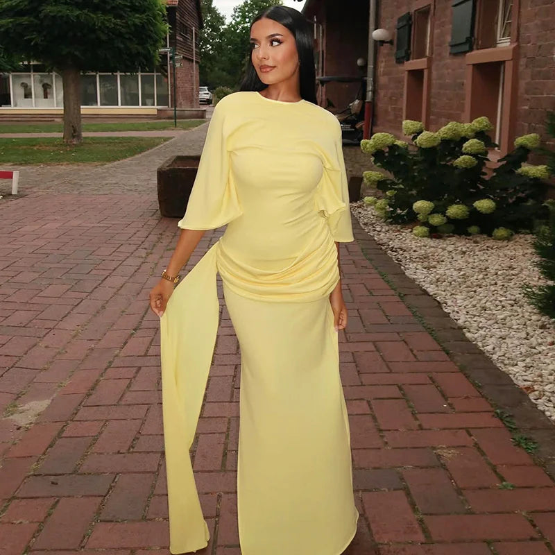 Woman in a yellow outfit walking on a brick path with greenery and a building in the background