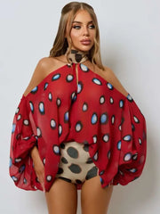 A woman modeling a red sheer off-the-shoulder top with a blue, black, and white spotted pattern, paired with beige leopard-print shorts, against a light gray background.