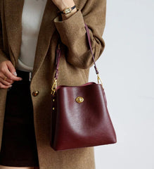 Person holding a maroon handbag with a gold clasp against a neutral background