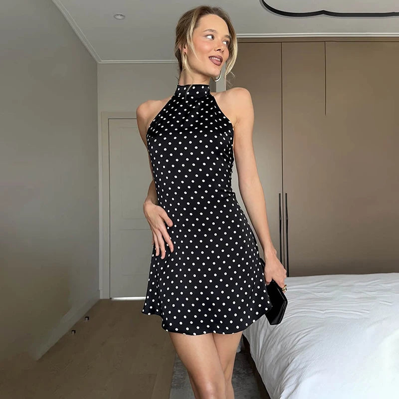 Woman wearing a black dress with white polka dots in a bedroom setting.