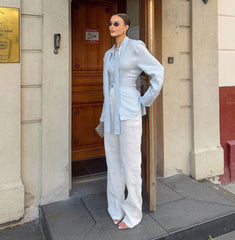 Woman in light blue jacket and white pants standing outside a building.