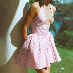 Woman wearing a pink checkered dress standing against a wall with a blurred outdoor background