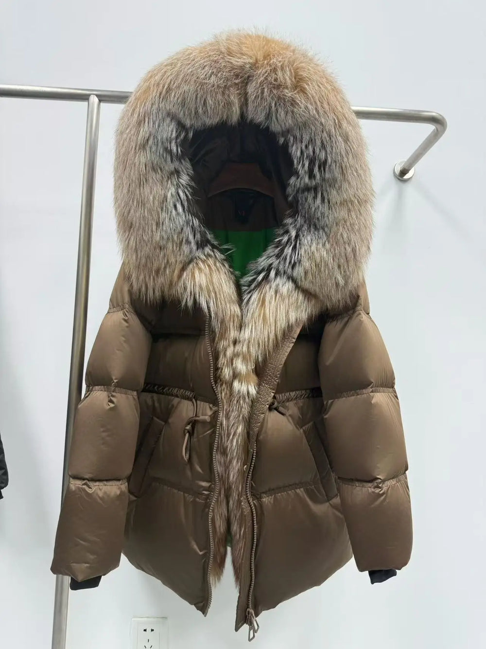 Brown puffer jacket with fur hood on a rack against a white background