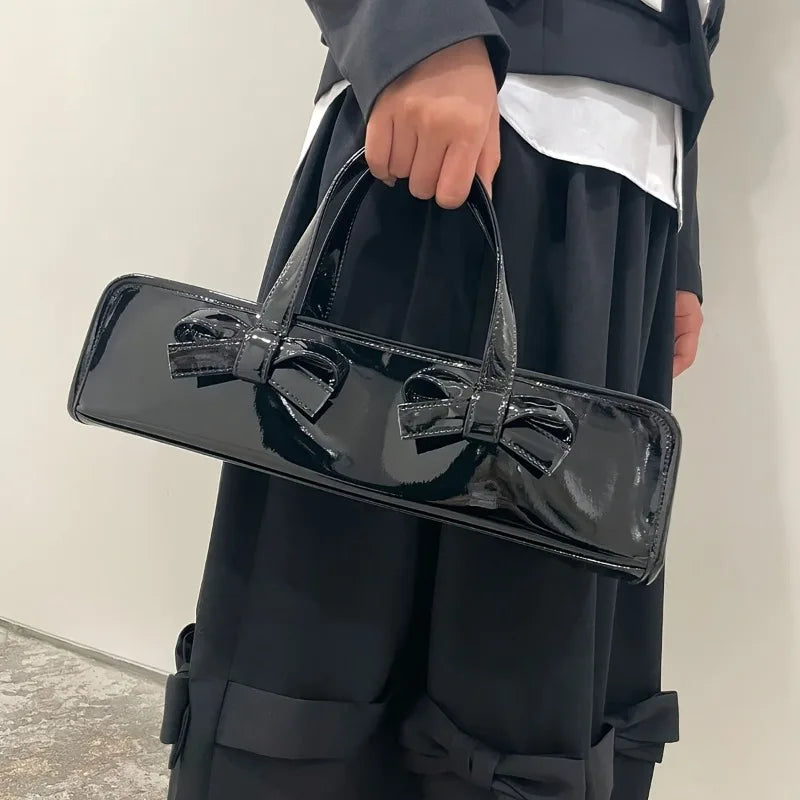 Black patent leather baguette bag with double bow detail carried by a person