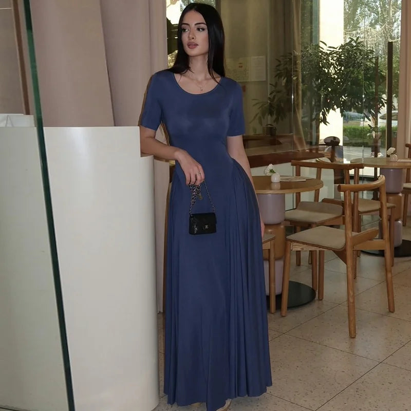 Woman in a blue dress standing in an indoor setting with tables and chairs.