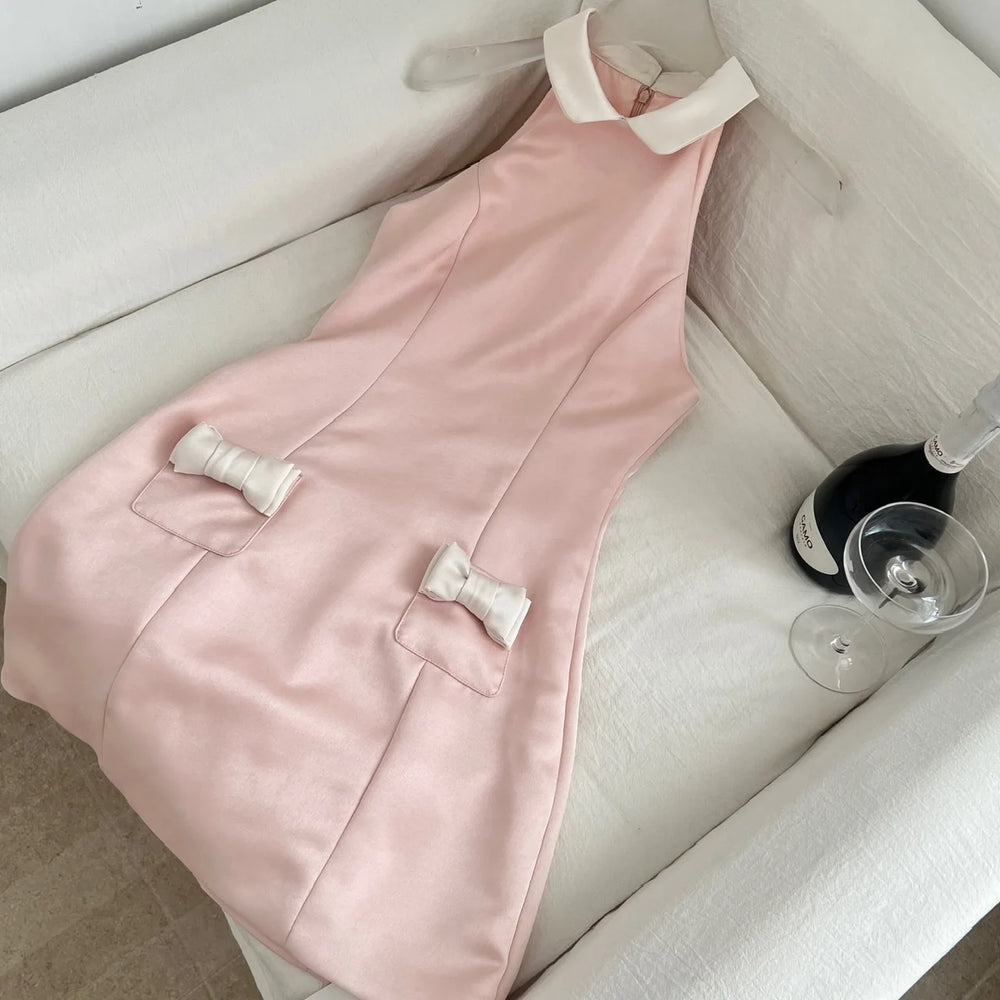 Pink satin halter neck mini dress with white collar and white bow pockets laid on a sofa