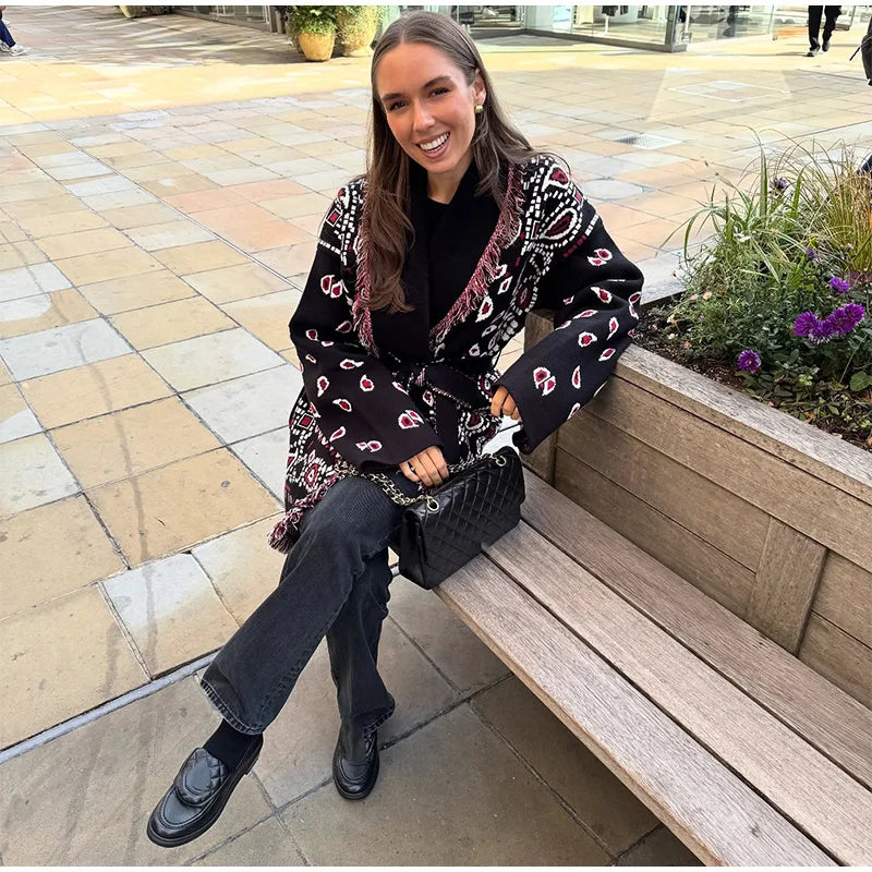 Woman sitting on a bench wearing a patterned coat, smiling at the camera.