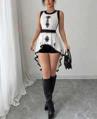 Woman wearing a black and white dress with floral embroidery, paired with black knee-high boots, standing against a neutral background.